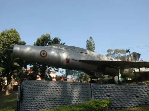 Chitralekha Udyan Tezpur display MiG-21 fighter aircraft Indian Air Force grey fuselage roundel red stripe trees blue sky concrete wall greenery, perfect aviation history park Tezpur Assam tour package.