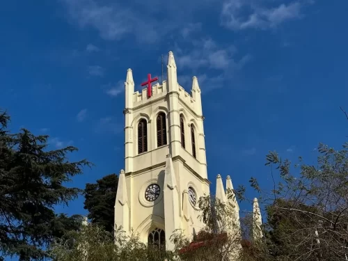Christ Church Shimla Neo-Gothic tower with red cross spires clock faces pine trees clear blue sky, iconic colonial landmark, Himachal Pradesh tour packages.