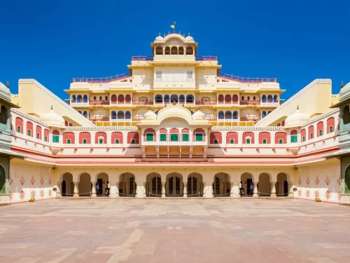 Iconic Chandra Mahal facade in central courtyard City Palace Jaipur Rajasthan with yellow towers pink arches green red wings open courtyard blue sky flags, perfect Rajasthan tour package