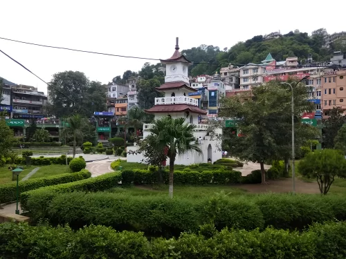 Clock Tower at Mandi Himachal Pradesh during misty afternoon, featuring white pagoda tower with palms amid town buildings and hills, perfect heritage experience Himachal Pradesh tour package.