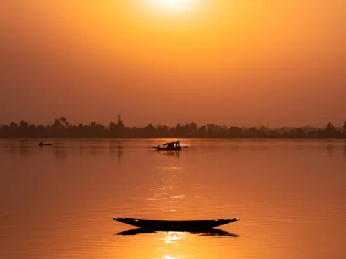 Dal Lake Srinagar Kashmir dramatic orange sunset silhouette shikara fishermen, houseboats hazy mountains golden reflections calm waters, perfect Jammu Kashmir Dal Lake sunset magic package.