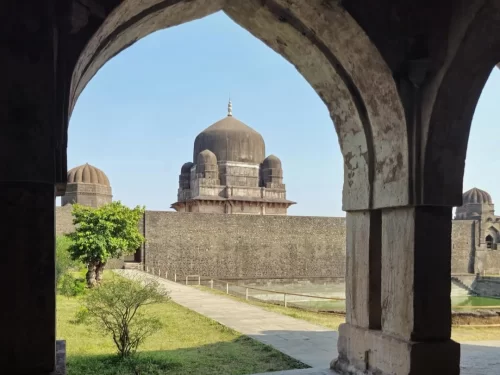 Darya Khan’s Tomb and Mosque in Mandu, Madhya Pradesh, viewed through a historic stone archway with its domed mausoleum and surrounding fort walls, a heritage site featured in Madhya Pradesh tour packages.