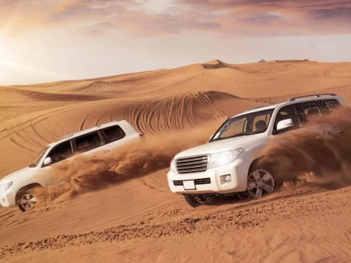 Desert Jeep safari thrilling dune bashing experience with powerful SUVs racing across golden sand dunes under a dramatic desert sky.