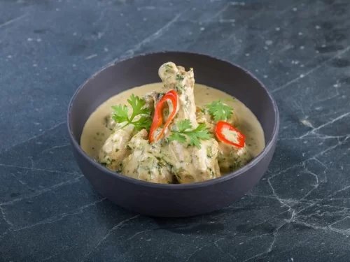 Dhaniwal Korma in creamy cilantro green gravy with red chili garnish, authentic Indian chicken korma, rich Indian cuisine delight.