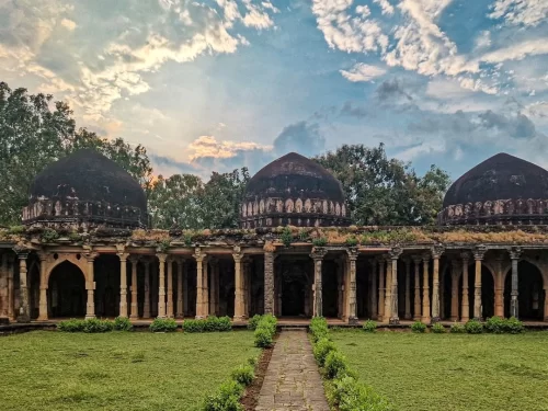 Dilawar Khan’s Mosque in Mandu, Madhya Pradesh, featuring three dark domes and a long arched colonnade courtyard under a dramatic evening sky, a historic highlight of Madhya Pradesh tour packages