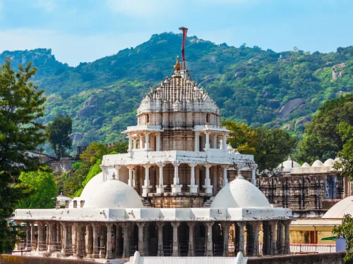Dilwara Jain Temple Mount Abu, featuring intricate white marble multi-tiered shikhara domes pillars forested hills blue skies flag, perfect Rajasthan tour packages.
