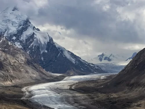 Snow peaks at Zanskar Valley during cloudy day, featuring glacier river, rugged mountains, perfect adventure experience with Ladakh Zanskar tour package.