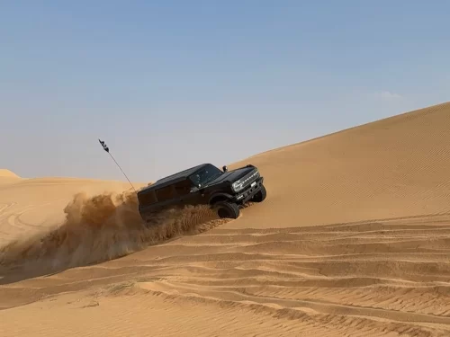 Dune Bashing powerful off road SUV speeding across golden desert dunes with sand spraying dramatically under a clear blue sky.