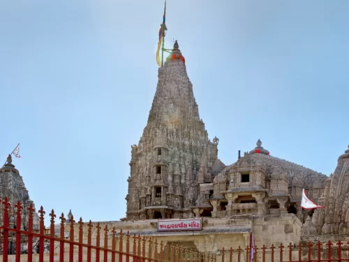 Dwarkadhish Temple in Dwarka during clear day, featuring towering multi-tiered shikhara with flags and red fence, perfect pilgrimage experience with Gujarat tour packages.