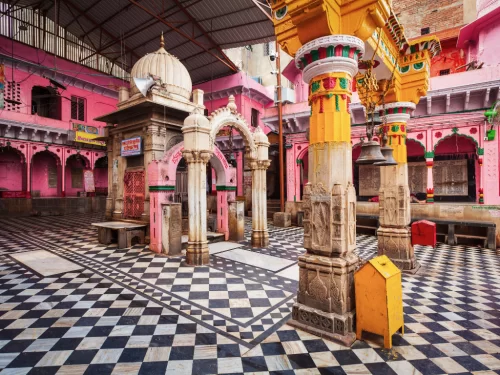 Shri Dwarkadhish Temple Kankroli Rajsamand Rajasthan pink haveli-style courtyard with ornate yellow pillars, carved arches, checkered black-white marble floor under metal roof, perfect Vaishnava heritage India tour package