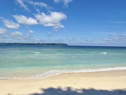 Panoramic Laxmanpur Beach Neil Island Andaman during sunny partly cloudy day, featuring white sands turquoise gradient lagoon offshore island palm shadows, perfect serene beach paradise Andaman tour package.