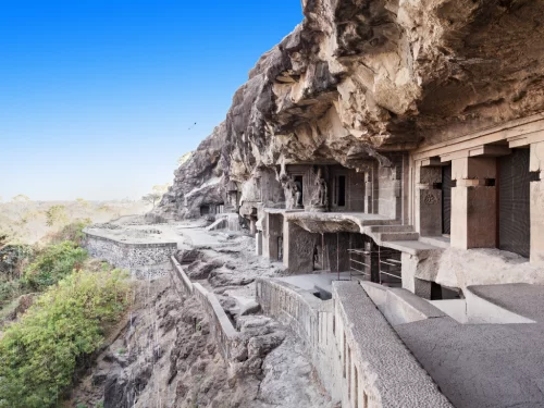 Rock-cut cave facades at Ellora Caves in Aurangabad during clear blue sky, featuring cliffside temples, greenery, perfect historical Aurangabad tour package. 