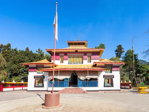 Colorful Enchey Monastery in Gangtok during sunny daytime, featuring Tibetan architecture, prayer flagpole and blue sky, perfect spiritual Sikkim tour package