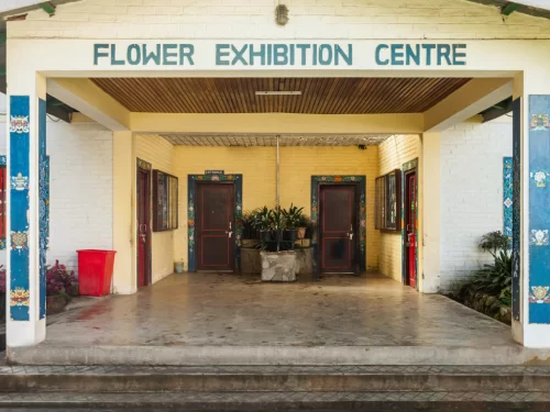 Entrance of Flower Exhibition Centre in Gangtok during daytime, featuring simple portico, potted plants and signage, ideal for floral sightseeing in Sikkim tour packages.