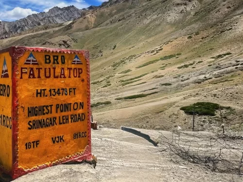 A vibrant yellow BRO sign marks the summit of Fotu La Pass at 13,479 feet, set against the sweeping, arid slopes and rugged peaks of the Himalayan landscape on the Srinagar-Leh highway.