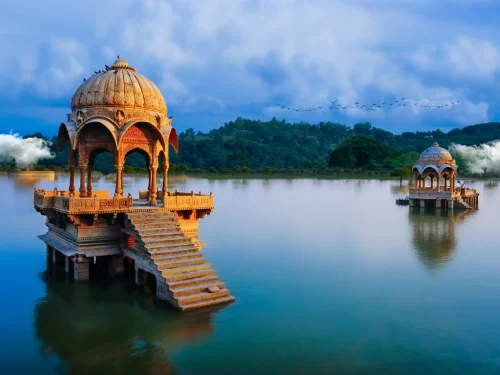 Gadisar Lake golden sandstone pavilion on lake pillars with stairs & birds under sunset clouds birds flying, perfect cultural heritage Jaisalmer Rajasthan tour packages.