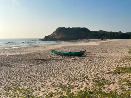 Ganeshgule Beach in Maharashtra featuring a quiet sandy shoreline with a traditional fishing boat and scenic coastal hills, a hidden Konkan gem often included in Maharashtra tour packages 