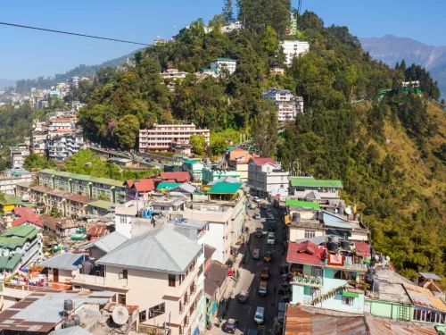 Gangtok city view from Gangtok Ropeway during clear daylight, featuring hillside buildings and winding road, perfect cityscape Sikkim tour package.