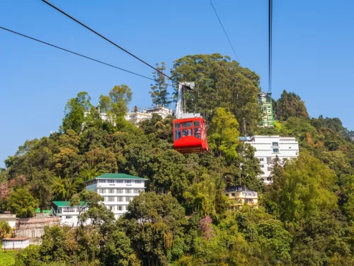 Gangtok Ropeway cable car gliding above forested hillside and town buildings during clear daylight, offering panoramic city and valley views, perfect family Sikkim tour package.
