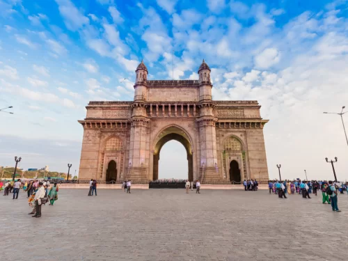Gateway of India wide-angle day view with tourists exploring the grand Indo-Saracenic arch under a vibrant blue sky, showcasing Mumbai’s iconic waterfront monument and popular sightseeing attraction.