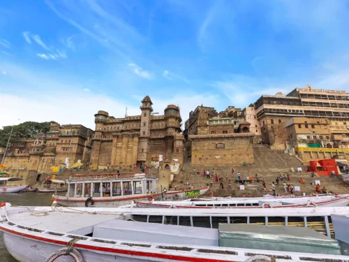 Munshi Ghat palace at Varanasi during clear day, featuring Darbhanga Ghat towers boats crowds, perfect cultural Uttar Pradesh tour package.