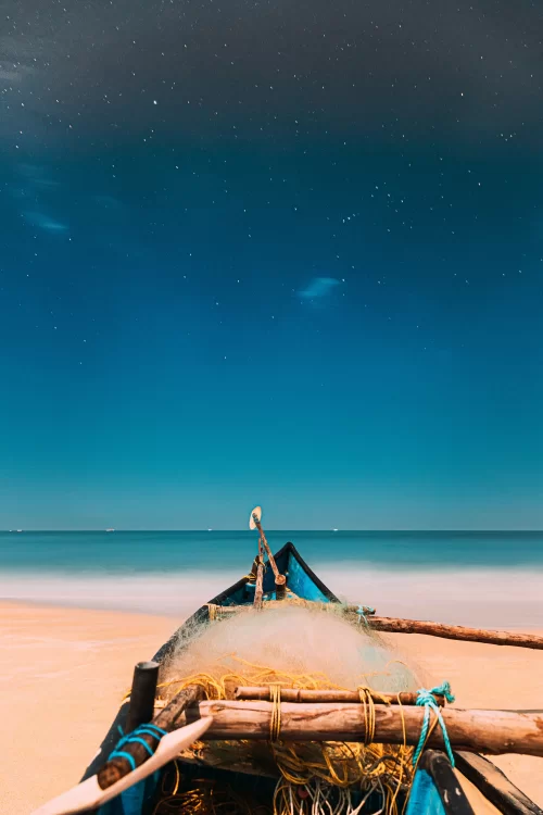 Fishing boat with nets resting on a quiet Goa beach under a starry night sky, a serene coastal experience featured in Goa tour packages.