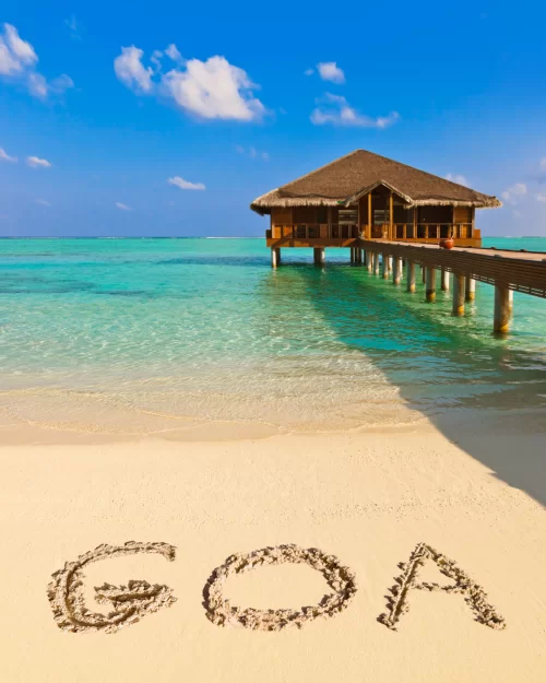 Overwater beach hut on clear turquoise sea with GOA written on soft white sand, a dreamy tropical holiday experience highlighted in Goa tour packages.