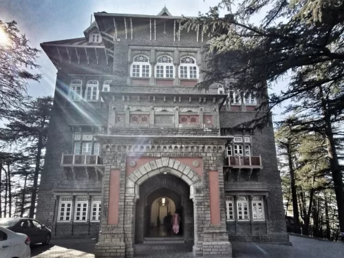 Gorton Castle in Shimla, Himachal Pradesh, a historic grey-stone colonial building with arched entrance, wooden balconies, and tall deodar trees, a heritage landmark featured in Himachal Pradesh tour packages.