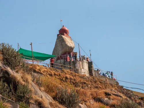 Guru Shikhar Mount Abu highest peak, featuring red-domed rock shrine devotees green tent railings arid hills blue skies, perfect Rajasthan tour packages.