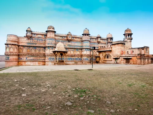 Man Mandir Palace at Gwalior Fort during clear afternoon, featuring turquoise tilework domes and intricate sandstone carvings, perfect heritage experience in Madhya Pradesh tour package.