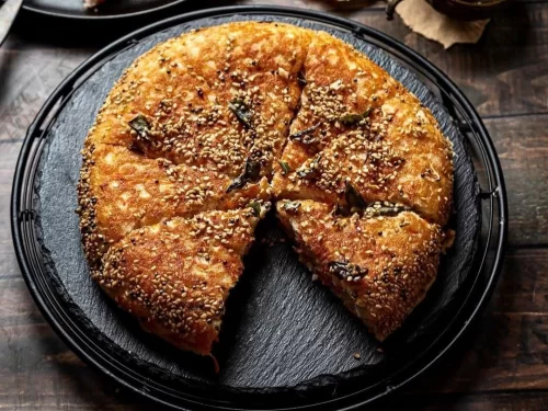 Handvo in savory lentil rice cake with sesame seed crust and herb garnish, authentic Indian Gujarati snack, warm Indian cuisine delight.