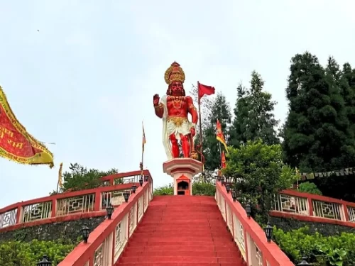 Large Hanuman Temple statue atop red stairway in Kalimpong, West Bengal, surrounded by greenery and temple flags, a prominent spiritual site featured in West Bengal tour packages.