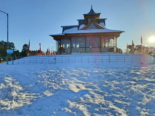 Hatu Mata Temple at Narkanda during winter sunrise, featuring snow blanket, red flags, prayer lamps, perfect spiritual Himachal Pradesh tour package.