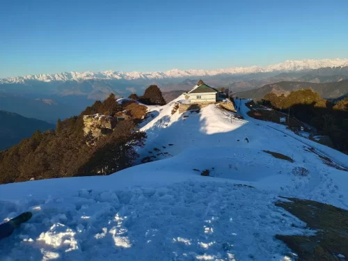 Hatu Peak Temple at Narkanda during winter sunrise, featuring white building, snowy ridges, distant Himalayas, pine trees, perfect adventure Himachal Pradesh tour package.