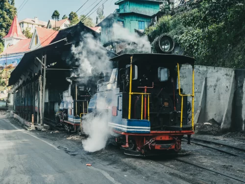 Darjeeling Himalayan Railway steam engines at shed during misty morning, featuring smoke, narrow gauge tracks and hillside town, perfect Sikkim tour package