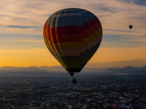 Hot Air Baloon ride over a city at sunrise with a colorful balloon floating above mountains and landscape.