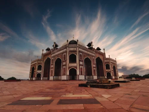 Humayun’s Tomb, Delhi – dramatic low-angle view of the Mughal red sandstone mausoleum and arches against a vibrant evening sky, iconic UNESCO World Heritage landmark for Delhi holiday packages