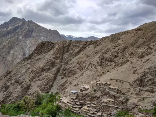 Hunderman Village Kargil Ladakh ghost settlement terraced on dramatic sheer cliff face under moody overcast skies, Brokpa stone houses amid rugged Karakoram peaks with distant snow, perfect LoC adventure India tour package.
