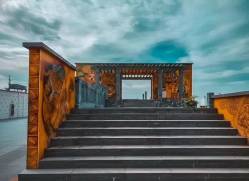 Iconic entrance gate at Samudra Beach Kovalam during overcast skies, featuring tribal murals, arched pergola, stone steps, perfect romantic experience with Kovalam tour package.