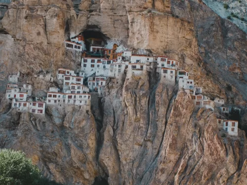 Zanskar Ladakh Phuktal Phugtal Gompa Buddhist cave monastery white buildings red roofs embedded rugged cliff cave entrance barren rocky Himalayan mountains landscape remote adventure trek pilgrimage tourism photography.