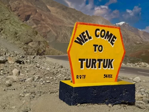 Welcome to Turtuk village signboard in Nubra Valley Ladakh during partly cloudy day, featuring R9TF unit marker, rugged mountains, perfect cultural Turtuk tour package. 