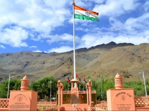 Drass Kargil War Memorial Ladakh pink sandstone Operation Vijay memorial arch Indian tricolor flag blue sky cloudy rugged mountains backdrop lanterns plaques trees, honoring 1999 Kargil heroes NH1D Ladakh adventure trek.