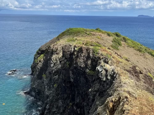 Cliff edge panorama at Chidiya Tapu Port Blair during partly cloudy day, featuring rocky outcrops, turquoise ocean, green vegetation, distant islands, perfect bird sanctuary adventure Andaman tour package.