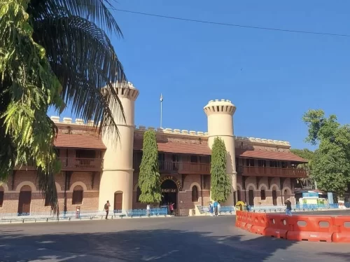 Main gate at Cellular Jail Port Blair Andaman during clear skies, featuring watchtowers, arched entrance, palm trees, colonial brickwork, perfect heritage experience Andaman tour package. 