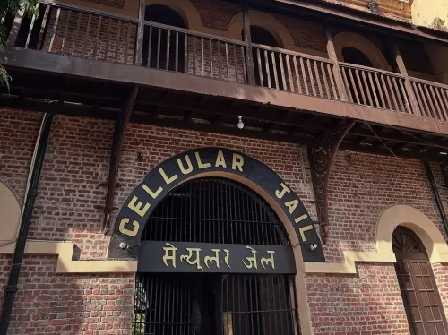 Main entrance at Cellular Jail Port Blair Andaman during clear skies, featuring arched gateway, iron gates, brick verandas, palm trees, perfect heritage experience Andaman tour package. 