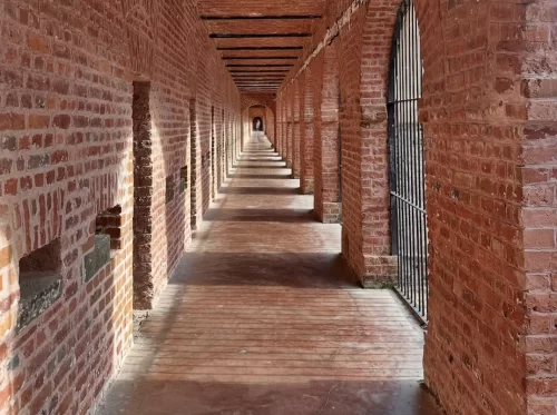 Cell corridor at Cellular Jail Port Blair Andaman during golden hour, featuring brick arches, iron bars, cell doors, shadows, perfect heritage experience Andaman tour package. 