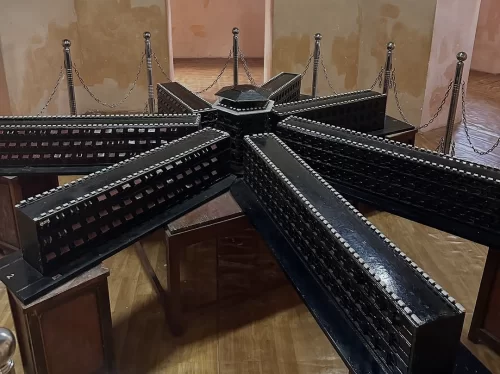 Scale model of Cellular Jail Port Blair Andaman at museum during indoor lighting, featuring seven-spoke wheel structure, chains, railings, perfect heritage experience Andaman tour package.