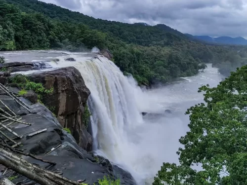 Athirappilly Waterfalls Thrissur Chalakudy Kerala India majestic powerful cascade plunging rocky cliff Chalakudy River lush green forested mountains misty spray cloudy skies foreground, perfect Kerala nature adventure wildlife tour package.