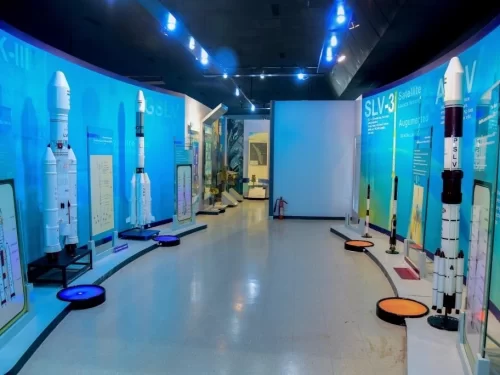 Vikram Sarabhai Space Centre Thiruvananthapuram ISRO museum interior GSLV SLV rocket models exhibits blue lighting display panels interactive screens curved walls LED floor lights educational gallery, space science tour package. 