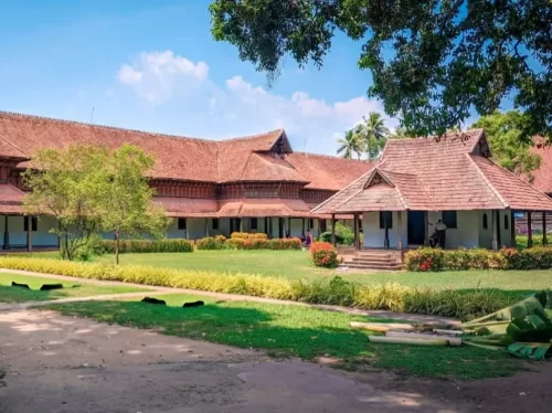 Kuthiramalika Palace Thiruvananthapuram Kerala traditional sloping terracotta roofs, ornate wooden pillars and lush tropical gardens under clear blue sky, perfect India tour package.